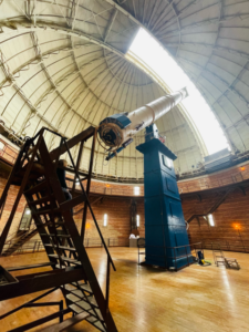 The Great Refractor telescope pointing at the sky through the dome's shutter with the telescope's staircase near the telescope.