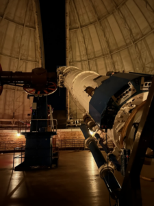 The Great Refractor telescope pointing at the night sky through the dome's shutter.