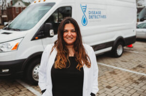 Dr. Sahar Alameh stands in front of a white van with Disease Detectives written on the side.