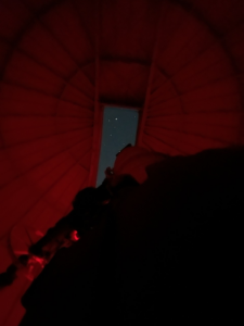 The Great Refractor telescope pointing at the night sky through the dome's shutter in red light.