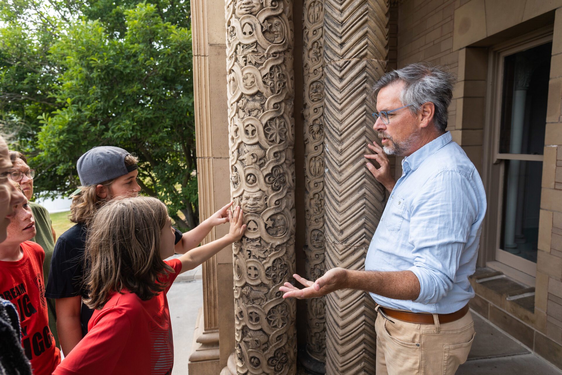A man and two children touching decorative carved columns.