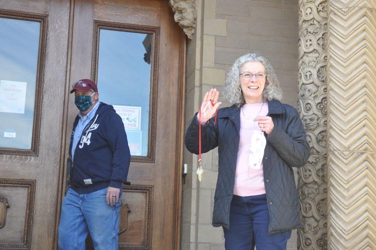 A woman holds a key on a keychain outside Yerkes Observatory with a man in the background.