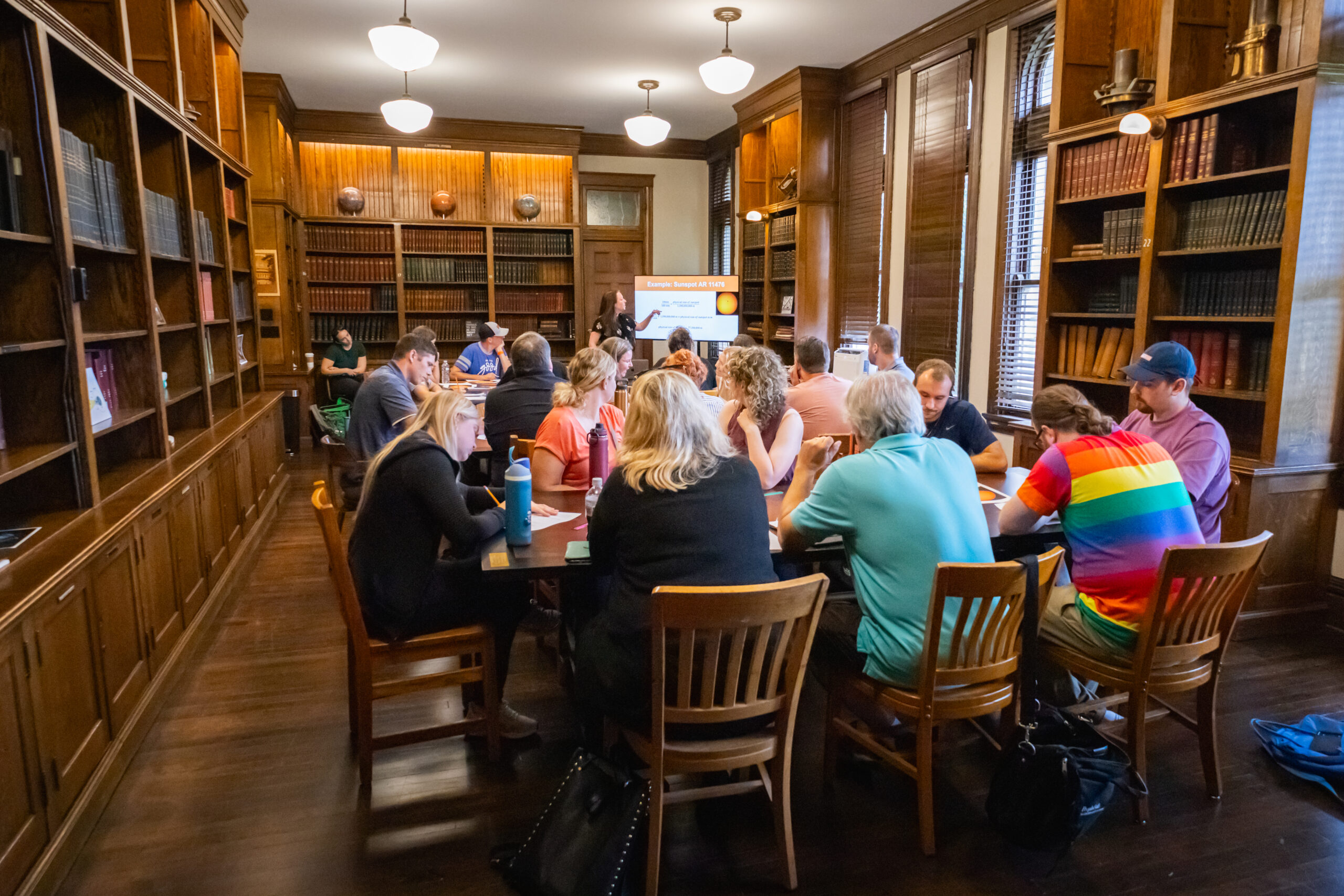 A group of people sitting around a large table in a wood-paneled library.