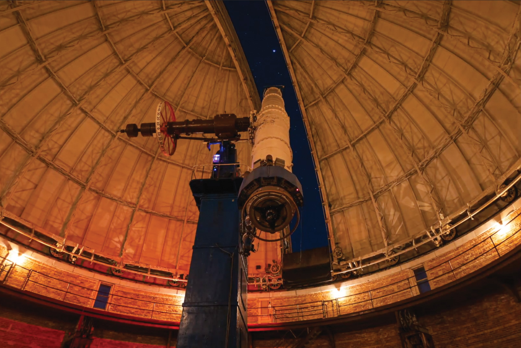 A telescope pointed out an opening in an observatory dome at night.