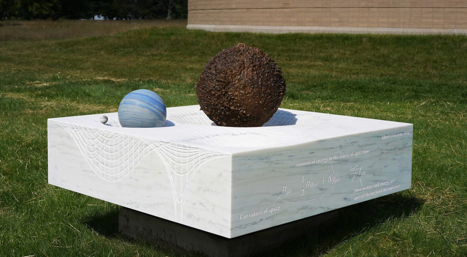 A sculpture with a brown sphere and a blue sphere on a large white marble square platform.