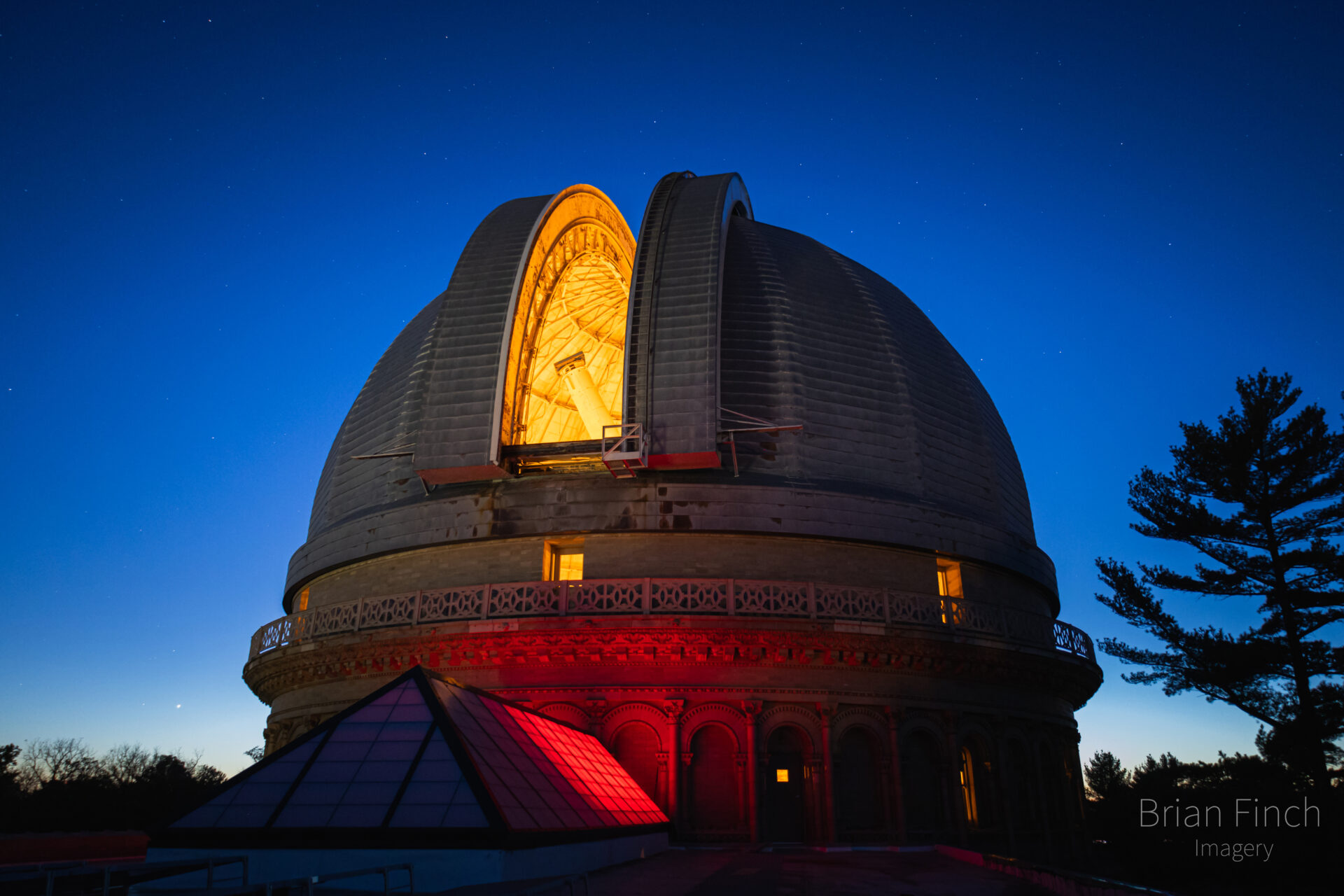 An observatory dome open at night with light shining from within.