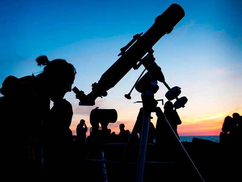 A person looking through a telescope at dusk.