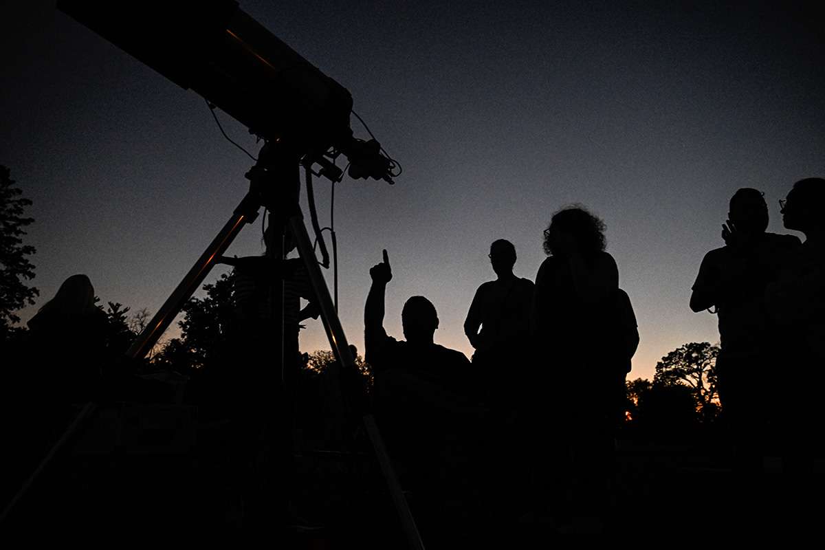 Silhouettes of a group of people and a telescope at dusk.