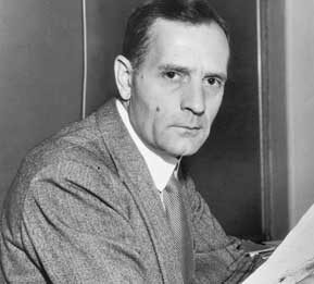 A black and white image of an unsmiling person in a grey suit holding an astronomical image.